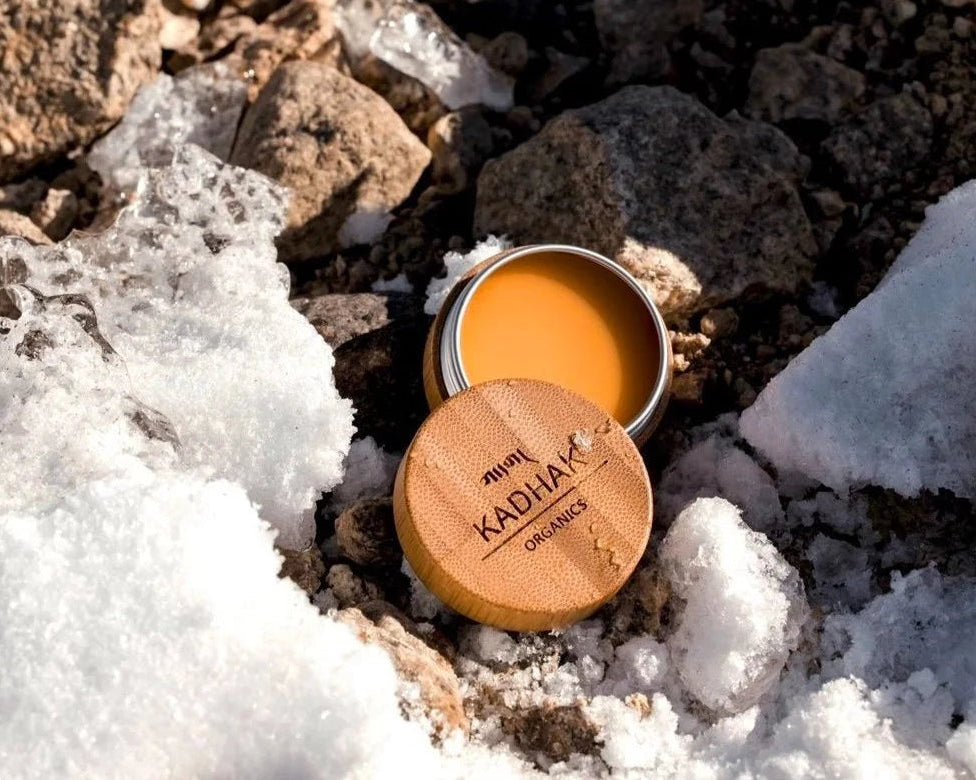 Open container of Kadiha Organics balm on a rocky surface with snow